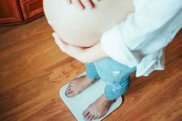 Image of woman weighing herself and experiencing weight gain through pregnancy East Kilbride